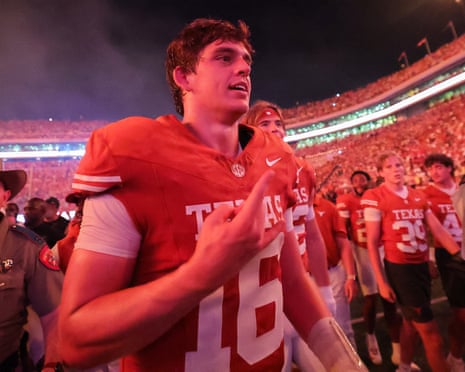 Arch Manning gestures while walking off the field in a packed stadium at night