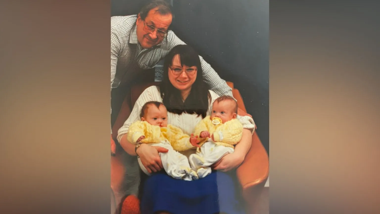 Family photo A family photo of a mum and a dad holding two babies. The mum is sitting down and the dad is crouched over the chair. The parents are smiling at the camera